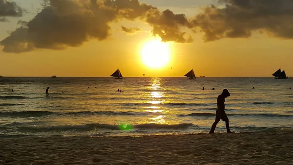 Sahilde yürüyen bir adam Denizde ve gün batımında.