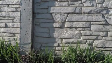 Arka plan dokusu çimentodan yapılmış gri çit. Ön planda doğal taşın ve yeşil çimlerin yazılışı var.