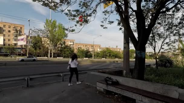 Chica en una camiseta blanca y zapatillas de deporte pasa cerca de la carretera con un tráfico de la ciudad ocupado — Vídeos de Stock