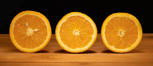 Naranjas sobre una mesa de madera y fondo negro, naranjas picadas, mitades de naranjas — Foto de Stock