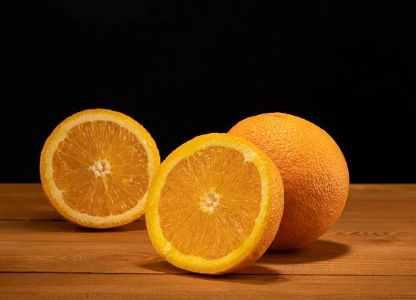 Mitad fresca y jugosa y rebanada de fruta naranja sobre una mesa de madera y fondo negro . — Foto de Stock