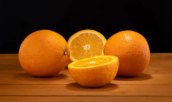 Frische und saftige Hälfte und Scheibe Orangenfrüchte auf einem Holztisch und schwarzem Hintergrund. — Stockfoto