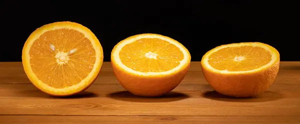Naranjas sobre una mesa de madera y fondo negro, naranjas picadas, mitades de naranjas — Foto de Stock