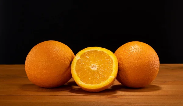 Mitad fresca y jugosa y rebanada de fruta naranja sobre una mesa de madera y fondo negro . — Foto de Stock