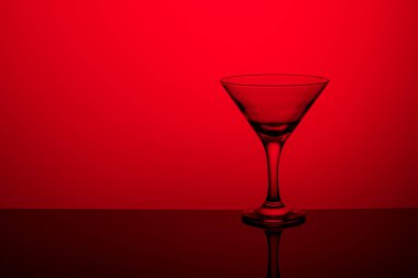 İnce bir bacakta şarapsız kadehler ayna yüzeyinde duruyor. Arka ışık. Kırmızı arkaplan.