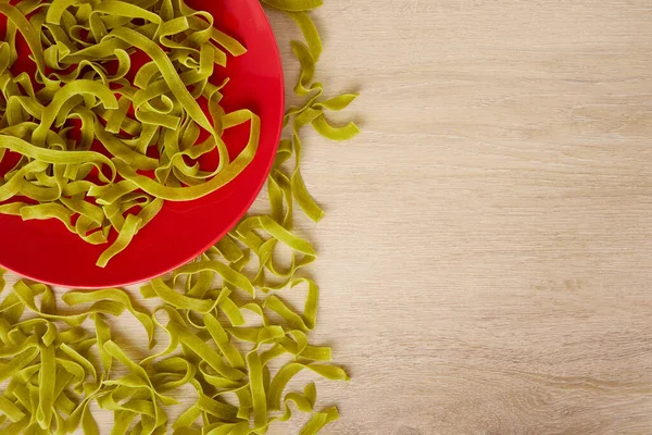 Pastas verdes crudas con espinacas en un plato rojo, vista superior, espacio para copiar — Foto de Stock