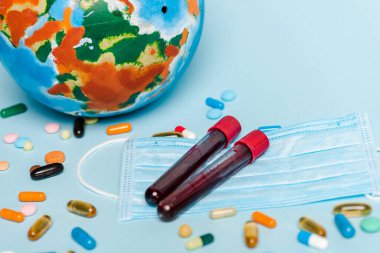 Tıbbi maskenin yanında kan örnekleri olan test tüpleri, mavi arka planda haplar ve küre, koronavirüs konsepti