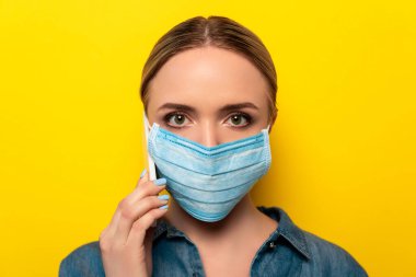 young woman in medical mask talking on smartphone on yellow background clipart