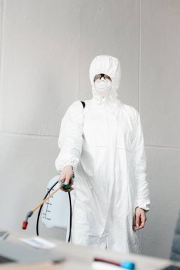Beyaz tehlikeli madde giysisi, solunum cihazı ve gözlük takan, ofisteki işyerlerini dezenfekte eden, koronavirüs konsepti