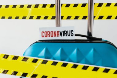 close up view of blue suitcase with coronavirus card in yellow and black hazard warning safety tape isolated on white clipart