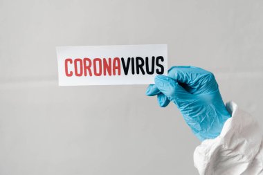 Elinde koronavirüs kartı olan lateks eldivenli birinin kırpılmış görüntüsü.