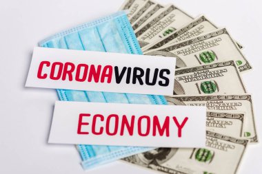 Dolar banknotları, tıbbi maske ve koronavirüs ve beyaz arka planda ekonomi kartları