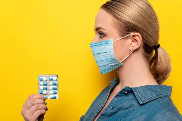 Visão Lateral Jovem Mulher Máscara Médica Segurando Pílulas Fundo Amarelo — Fotografia de Stock