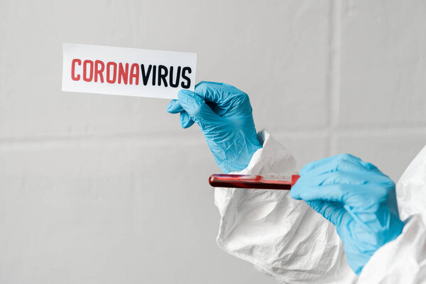 cropped view of person in latex gloves holding coronavirus card and blood sample