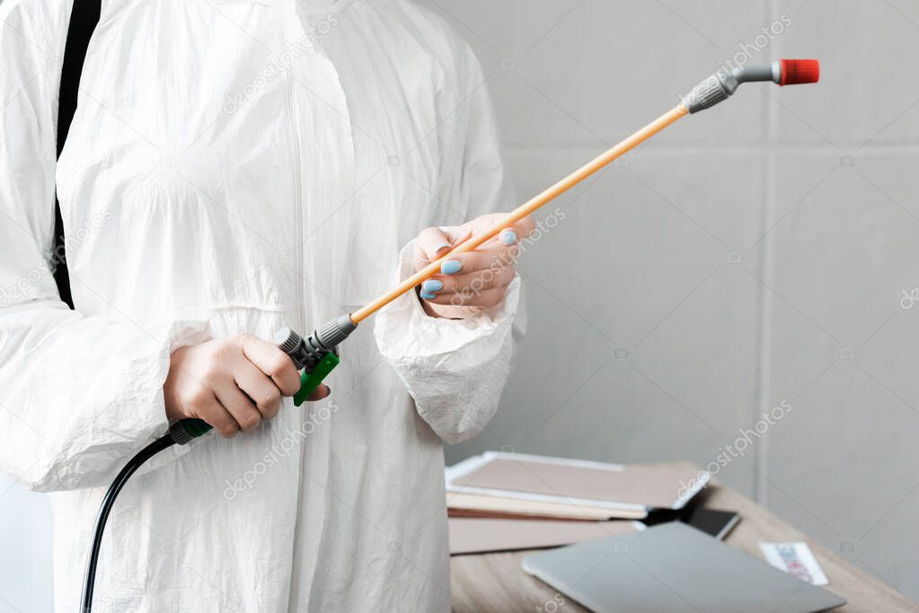 cropped view of person in white hazmat suit holding disinfect in office, coronavirus concept