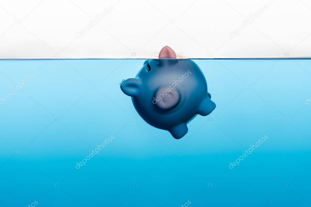 piggy bank going under blue water isolated on white, coronavirus crisis concept