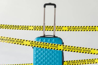 Sarı ve siyah tehlike bantlı mavi bavul. Beyaz, koronavirüs kavramına izole edilmiş karantina bölgesi illüstrasyonlu güvenlik bandı.