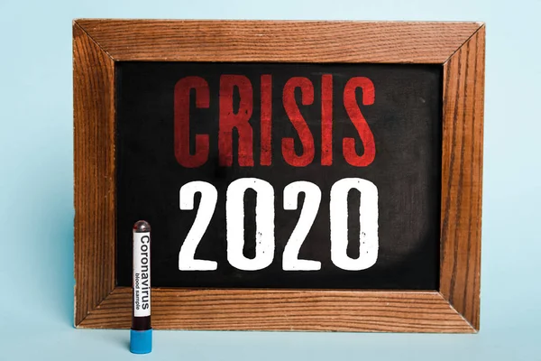 Kriz 2020 yazı tahtasında mavi arka planda Coronavirus kan örneğiyle test tüpünün yanında yazılmış.