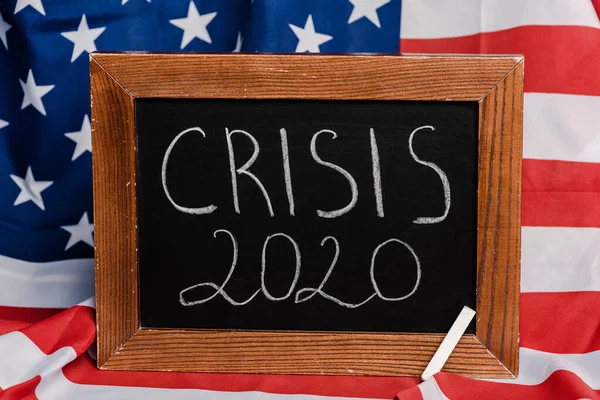 Crisis 2020 lettering written on chalkboard on american flag background, coronavirus concept — Stock Photo