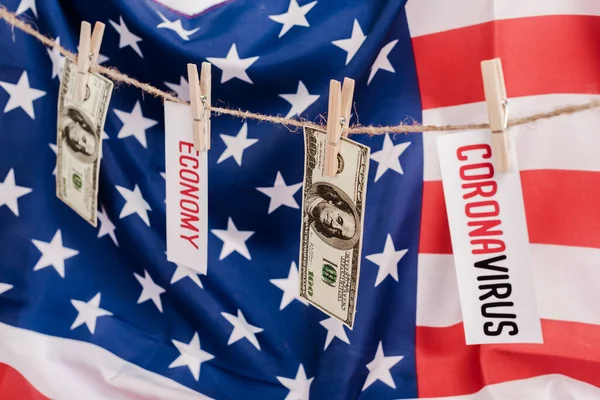 Dollar banknotes and cards with economy and coronavirus lettering hanging on rope on american flag background — Stock Photo