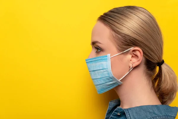 Vue latérale de la jeune femme en masque médical sur fond jaune, concept de coronavirus — Photo de stock