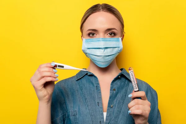 Jeune femme en masque médical tenant thermomètre et éprouvette avec échantillon de sang de coronavirus — Photo de stock