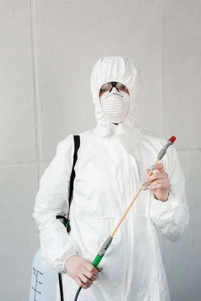 Person in weißem Schutzanzug, Atemschutzmaske und Schutzbrille mit Desinfektionsmittel im Büro, Coronavirus-Konzept — Stockfoto