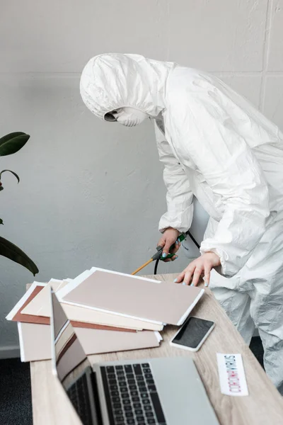 Persona en traje de materiales peligrosos blancos, respirador y gafas desinfectando el lugar de trabajo en la oficina, concepto coronavirus - foto de stock