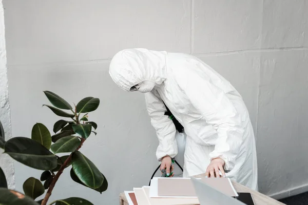 Person in weißem Warnanzug, Atemschutzmaske und Schutzbrille zur Desinfektion des Arbeitsplatzes im Büro, Coronavirus-Konzept — Stockfoto