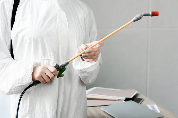 Vista recortada de la persona en traje de hazmat blanco que sostiene desinfección en la oficina, concepto coronavirus - foto de stock