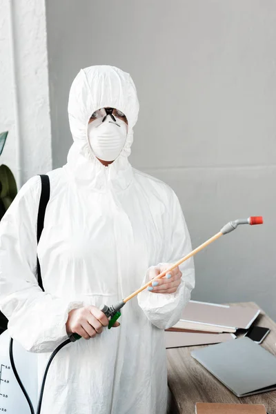 Person in weißem Warnanzug, Atemschutzmaske und Schutzbrille zur Desinfektion des Arbeitsplatzes im Büro, Coronavirus-Konzept — Stockfoto
