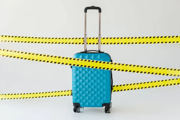 Blue suitcase in yellow and black hazard warning safety tape on white, coronavirus concept — Stock Photo