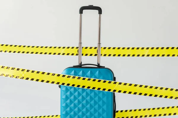 Blue suitcase in yellow and black hazard warning safety tape isolated on white, coronavirus concept — Stock Photo