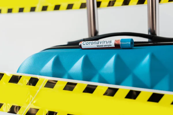 Vue rapprochée de la valise bleue avec échantillon de sang de coronavirus dans un ruban jaune et noir d'avertissement de danger isolé sur du blanc — Photo de stock