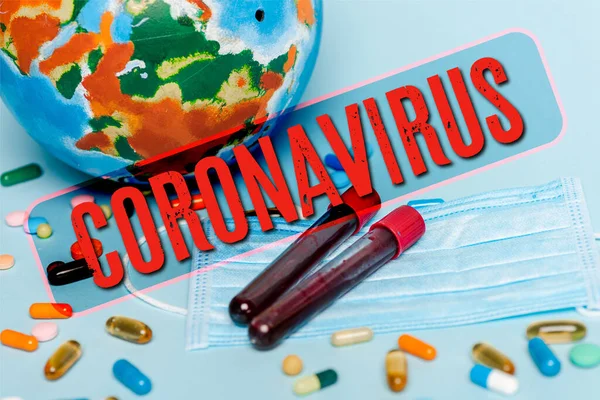 Éprouvettes avec des échantillons de sang près du masque médical, pilules et globe sur fond bleu, illustration de coronavirus — Photo de stock