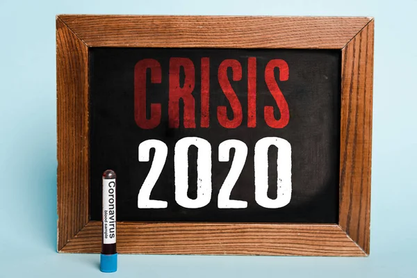 Crise 2020 lettering escrito em quadro-negro perto do tubo de ensaio com amostra de sangue coronavírus em fundo azul — Fotografia de Stock