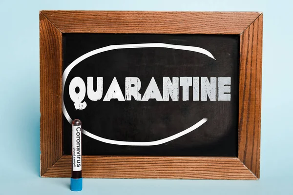 Quarantine lettering written on chalkboard near test tube with coronavirus blood sample on blue background — Stock Photo
