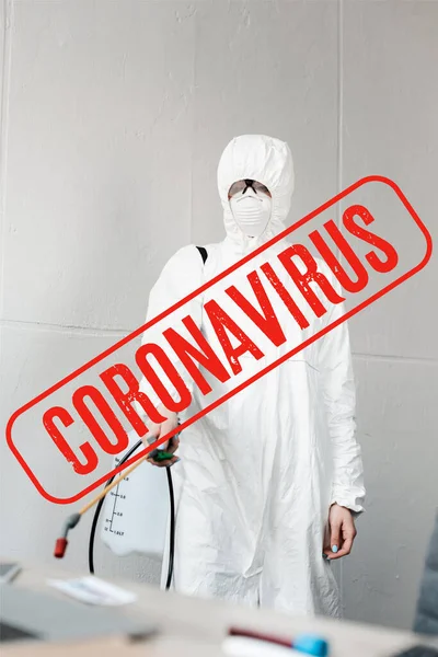 Foco seletivo da pessoa em terno branco hazmat, respirador e óculos desinfecção local de trabalho no escritório, ilustração coronavírus — Fotografia de Stock