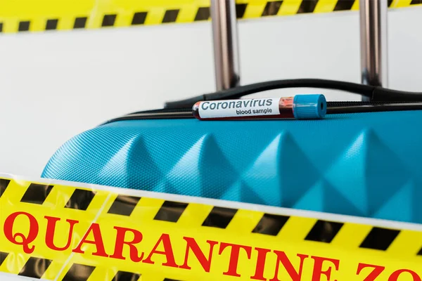 Nahaufnahme eines blauen Koffers mit Coronavirus-Blutprobe in gelbem und schwarzem Gefahrenwarnband mit Quarantäne-Illustration isoliert auf weiß — Stockfoto