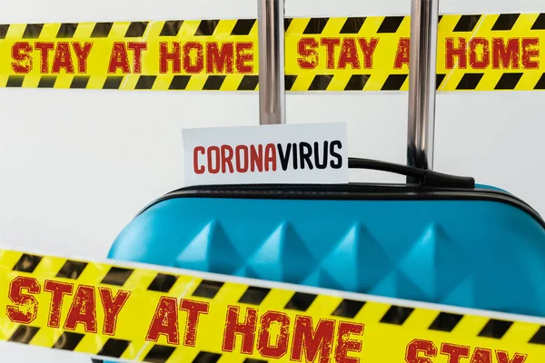 Close up view of blue suitcase with coronavirus card in yellow and black hazard warning safety tape with stay at home illustration isolated on white — Stock Photo