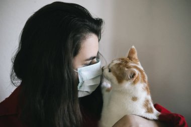 Tıbbi maskeli, kedili bir kız.