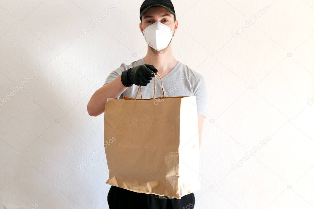 Food and goods delivery during the coronavirus pandemic. Deliveryman in uniform. The deliveryman is holding a bag of craft paper. Man in protective medical mask and rubber gloves.