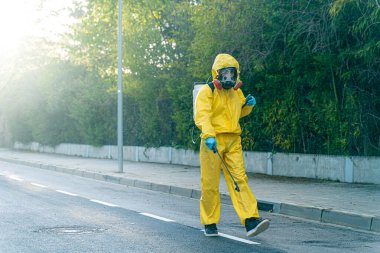 Coronavirus. Maske takıp sokakları temizleyen bir temizlik işçisi. Şehirdeki dezenfekte edilmiş şehirleri sterilize et. Coronavirüs 'e karşı dezenfekte. Kıyafet koruması. 