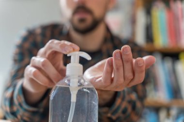 Coronavirus. Koruyucu maske takan bir adam evde çalışıyor. Koronavirüs için koruyucu maske takarak karantina. Evden çalışıyorum. Ellerini dezenfektan jeliyle temizliyor. Termometre ateşi denetimi.