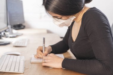 Coronavirus. Ofisteki Corona virüsü maskesi olan hasta bir kadın. İş kadınları sağlıklarını korumak ve korumak için maske takarlar. Evde bilgisayarla çalışıyor. Evden çalışmak. 