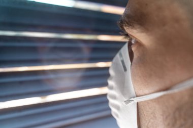 Coronavirus. Corona virüsünün hasta adamı pencereden dışarı bakıyor ve maske takıyor ve evdeki hastalıktan korunuyor. Karantinaya alın. Hasta enfeksiyonu önlemek için izole edilmiş. Pandemia. Ev.