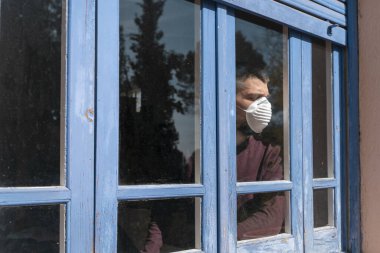 Coronavirus. Corona virüsünün hasta adamı pencereden dışarı bakıyor ve maske takıyor ve evdeki hastalıktan korunuyor. Karantinaya alın. Hasta enfeksiyonu önlemek için izole edilmiş. Pandemia. Ev.