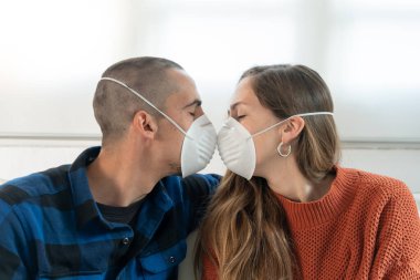 Coronavirus. Evde karantinada kanepede oturup televizyon izleyen bir çift. Kanepede oturan çift bulaşıcı hastalıktan korunmak için maske takıyor. Evde kal.. 