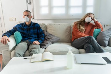 Coronavirus. Evde karantinada kanepede oturup televizyon izleyen bir çift. Kanepede oturan çift bulaşıcı hastalıktan korunmak için maske takıyor. Evde kal.. 