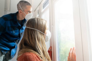 Coronavirus. Hasta bir çift korona virüsü pencereden dışarı bakıyor ve maske takıyor ve evdeki hastalıktan korunuyor. Karantinaya alın. Hasta enfeksiyonu önlemek için izole edilmiş. Ev.
